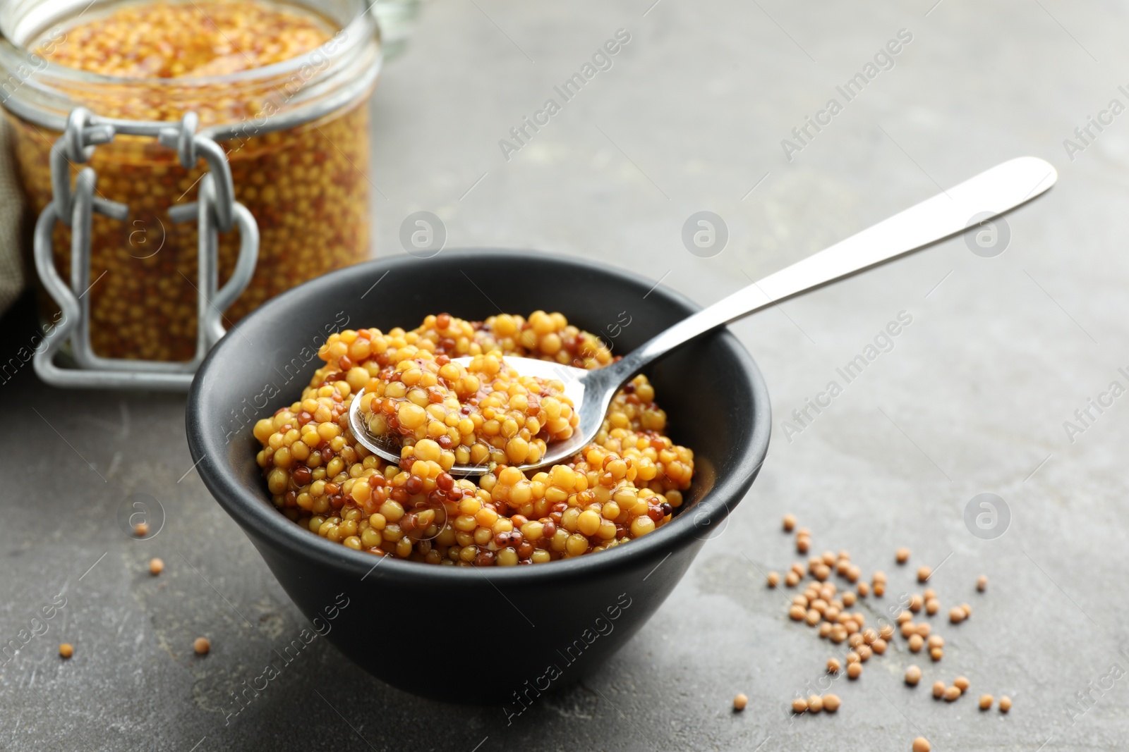 Photo of Whole grain mustard in bowl, spoon and dry seeds on grey table