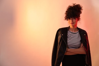 Beautiful young woman in black leather jacket posing on color background in neon lights. Space for text