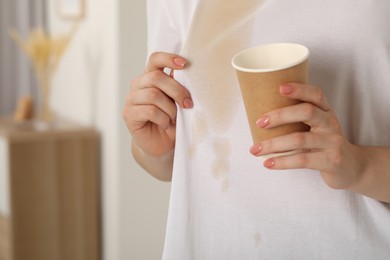 Woman showing stain from coffee on her shirt indoors, closeup. Space for text