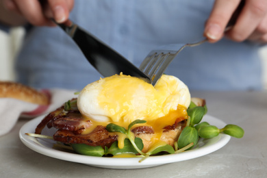 Photo of Woman eating tasty egg Benedict at table, closeup
