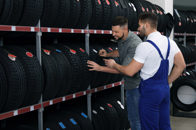 Mechanic helping client to choose car tire in auto store