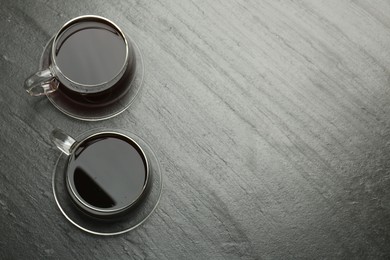 Photo of Hot coffee in cups on dark textured table, top view. Space for text