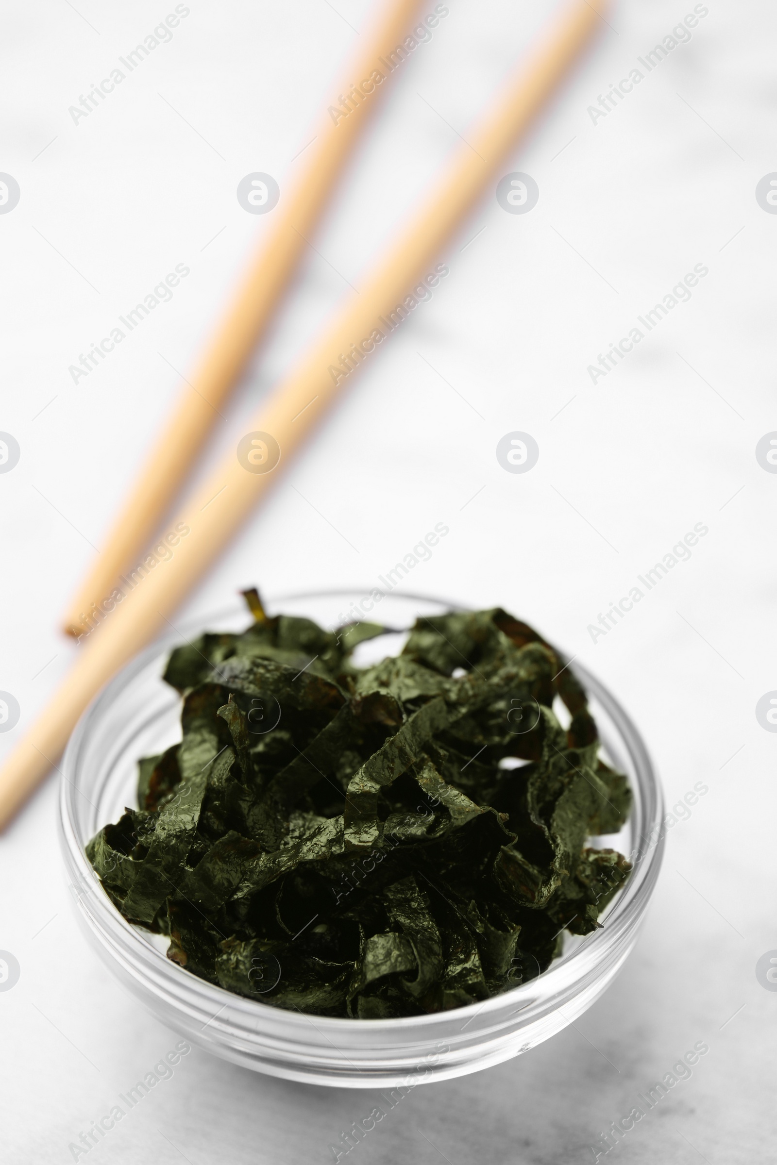 Photo of Chopped nori sheets with chopsticks on white marble table, closeup