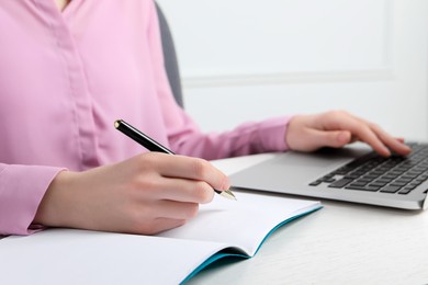 Woman with pen, notepad and laptop at white wooden table, closeup