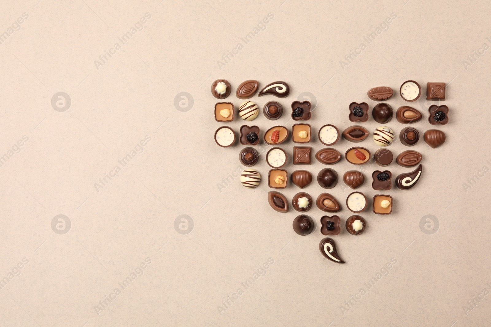 Photo of Heart made with delicious chocolate candies on beige background, top view. Space for text