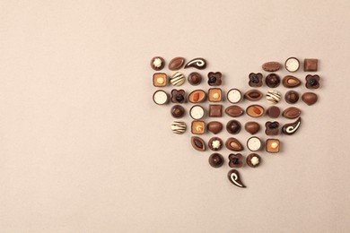 Heart made with delicious chocolate candies on beige background, top view. Space for text