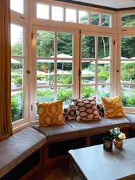 Photo of Wooden table near bay window seat with cushions in cozy room. Interior design