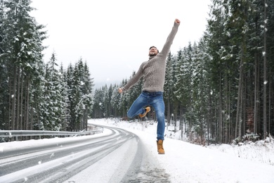 Photo of Emotional man jumping near snowy forest. Winter vacation