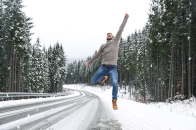 Emotional man jumping near snowy forest. Winter vacation