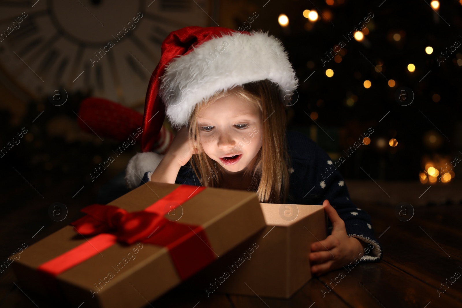 Photo of Cute child opening magic gift box near Christmas tree at night