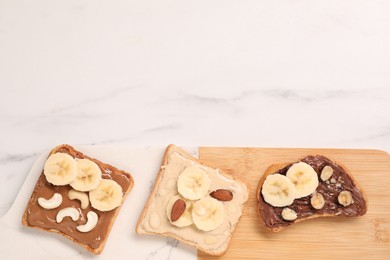 Toasts with different nut butters, banana slices and nuts on white marble table, flat lay. Space for text