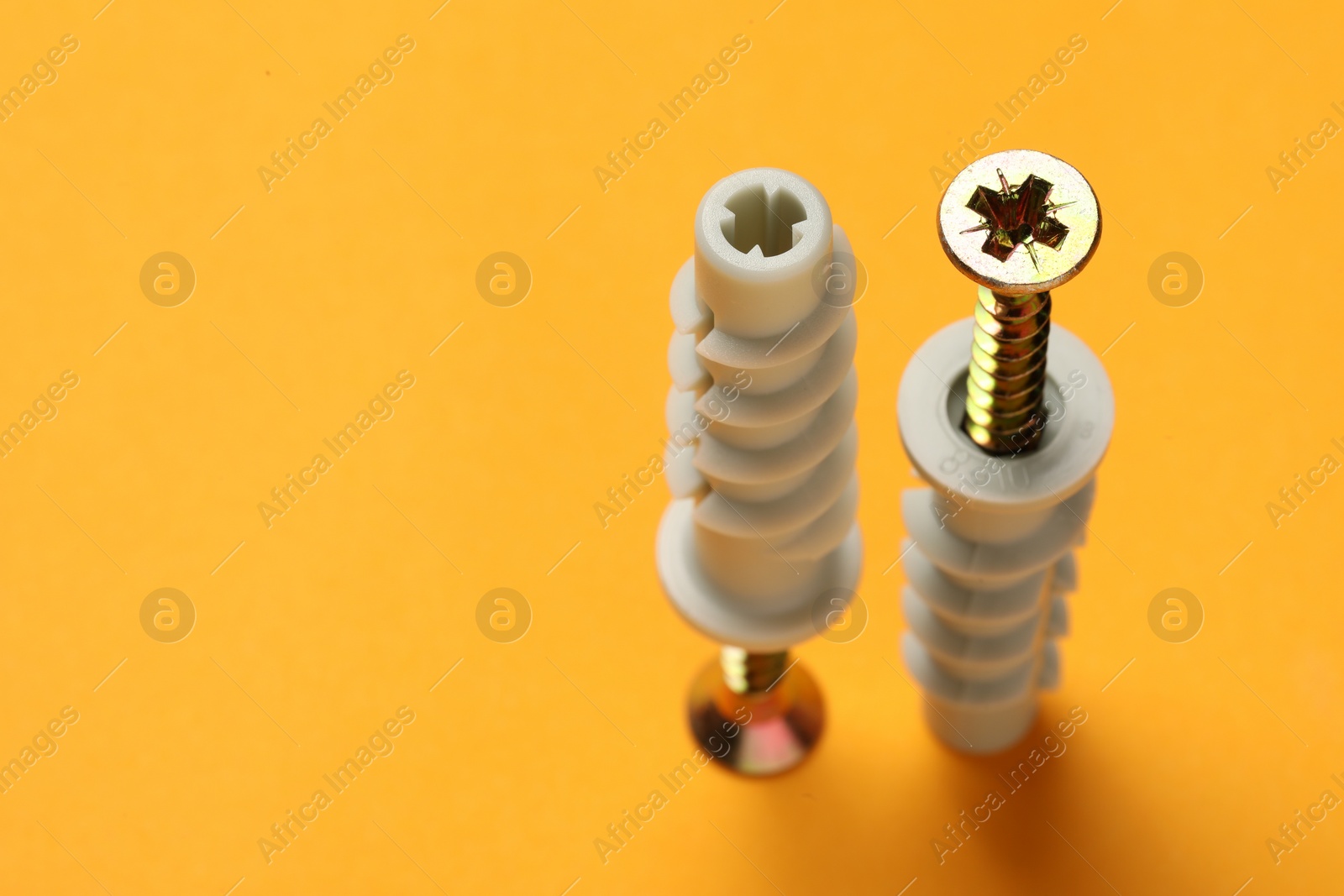 Photo of Metal screws with dowels on orange background. Space for text