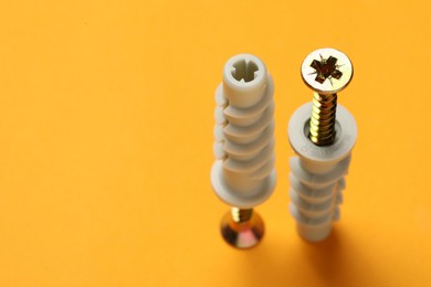 Metal screws with dowels on orange background. Space for text