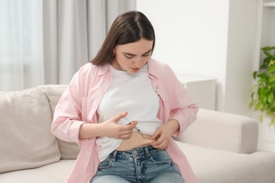 Photo of Diabetes. Woman making insulin injection into her belly on sofa at home