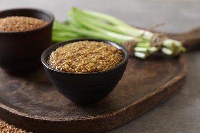 Photo of Serving board with delicious whole grain mustard, seeds and fresh green onion on grey table, closeup