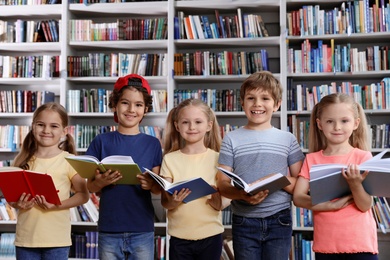 Photo of Group of little children reading books near shelves in library