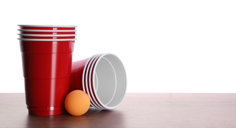 Photo of Plastic cups and ball for beer pong on wooden table against white background