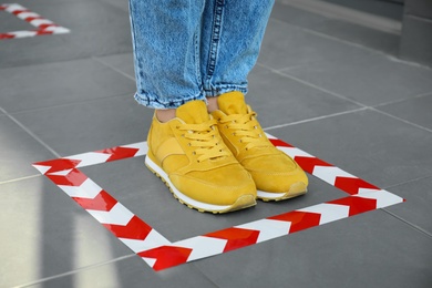 Photo of Woman standing on taped floor marking for social distance, closeup. Coronavirus pandemic