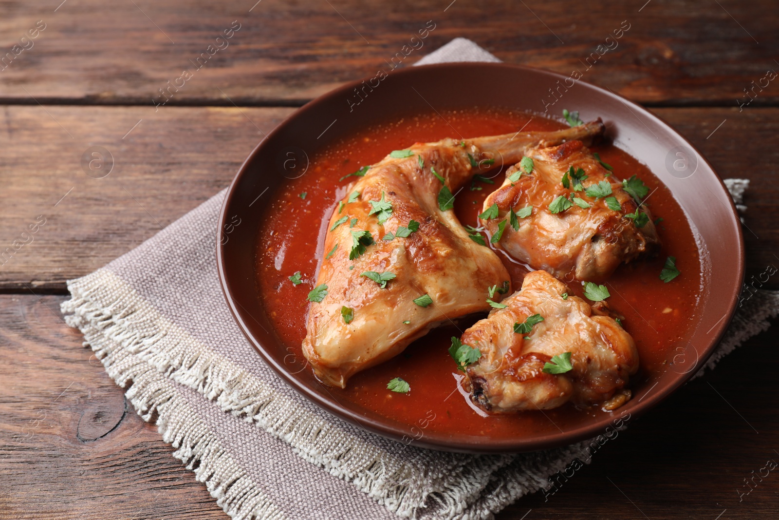 Photo of Tasty cooked rabbit meat with sauce and parsley on wooden table