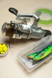 Different fishing baits and reel with line on light wooden table