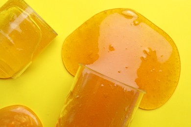 Photo of Overturned plastic containers with bright slimes on yellow background, top view