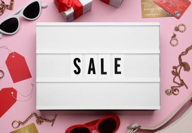 Lightbox with word Sale, credit cards and fashionable accessories on pink background, flat lay