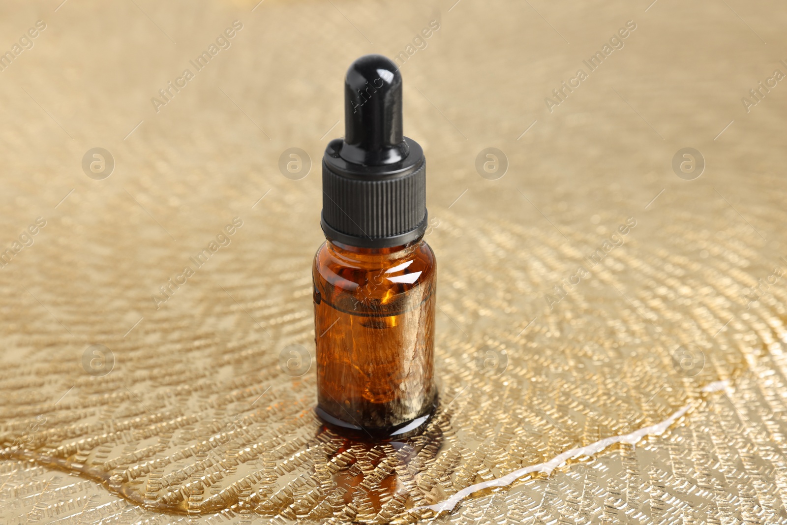 Photo of Bottle with oil on wet textured golden surface. Natural cosmetics