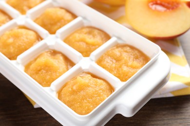 Photo of Nectarine puree in ice cube tray and fresh nectarine fruits on wooden table, closeup