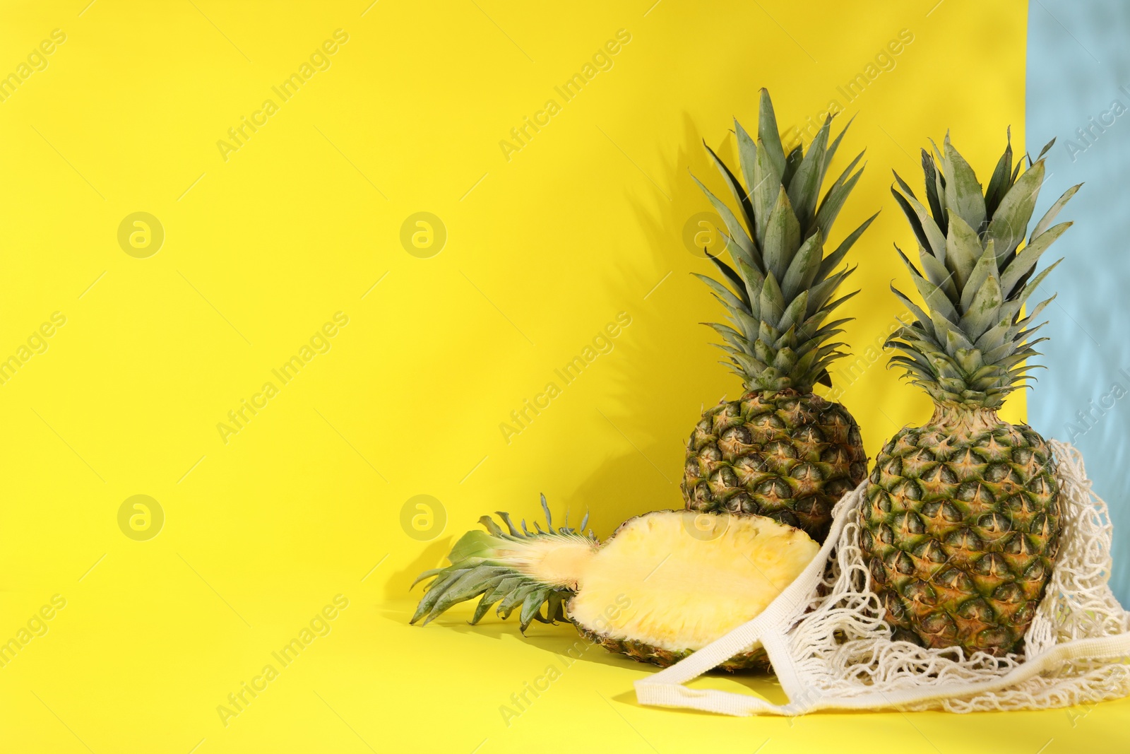 Photo of Whole and cut ripe pineapples on yellow background, space for text