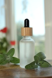 Photo of Bottle of mint essential oil and fresh herb on wooden table indoors
