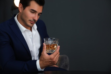 Young man with glass of whiskey on dark background. Space for text