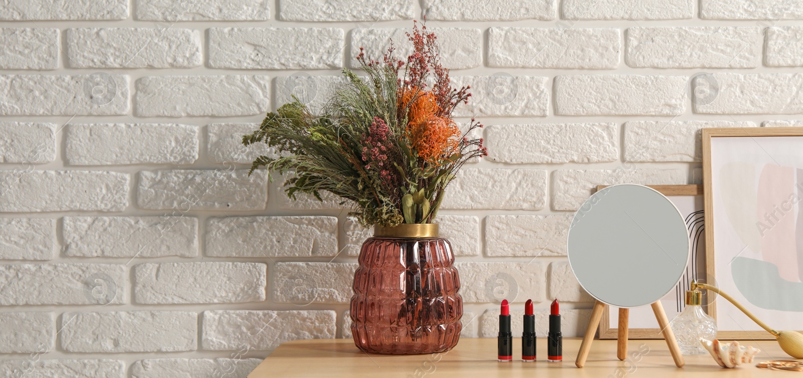 Image of Makeup room. Mirror, cosmetic products, perfume and vase with dried flowers on wooden dressing table indoors, space for text. Banner design