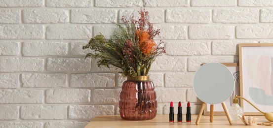 Makeup room. Mirror, cosmetic products, perfume and vase with dried flowers on wooden dressing table indoors, space for text. Banner design