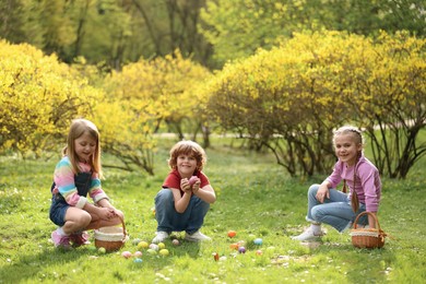 Photo of Easter celebration. Cute little children hunting eggs outdoors