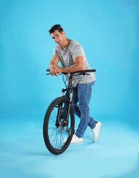 Handsome young man with modern bicycle on light blue background