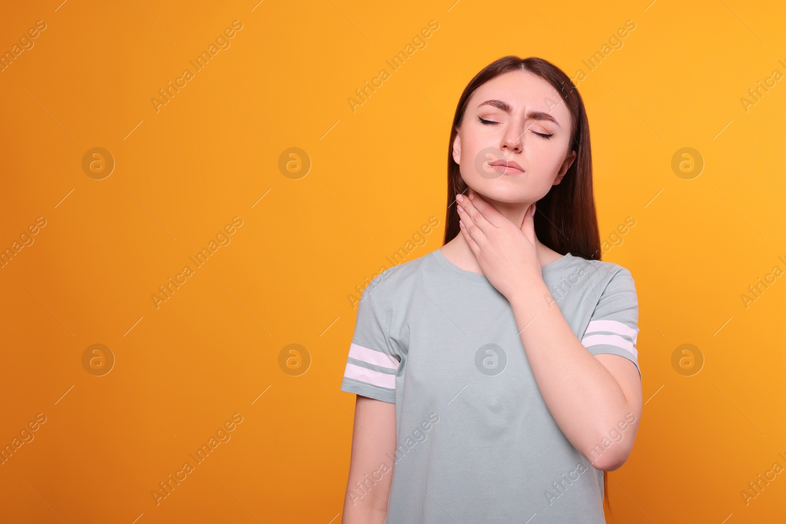 Photo of Young woman with sore throat on orange background. Space for text