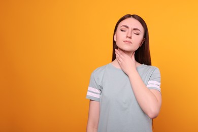 Young woman with sore throat on orange background. Space for text