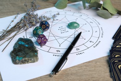 Photo of Zodiac wheel with sign triplicities, pen, gemstones and astrology dices on wooden table, closeup