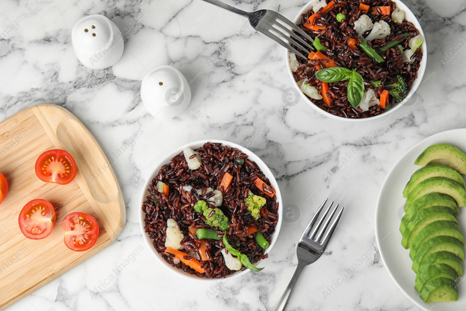 Photo of Bowls of brown rice with vegetables on marble table, flat lay