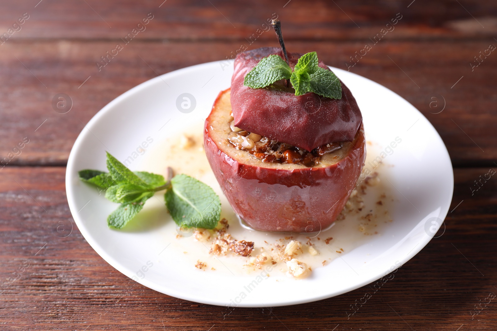 Photo of Tasty baked apple with nuts, honey and mint on wooden table, closeup