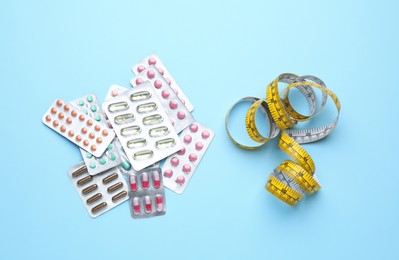 Photo of Many different weight loss pills and measuring tape on light blue background, flat lay