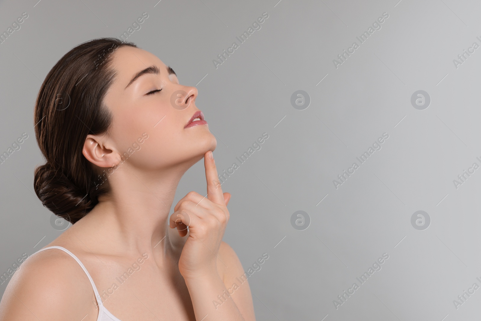 Photo of Young woman massaging her face on grey background. Space for text