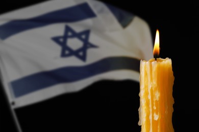 Image of Burning candle against flag of Israel on black background