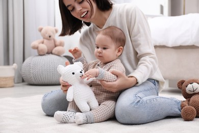 Photo of Cute baby and mother playing with toy bear on floor at home