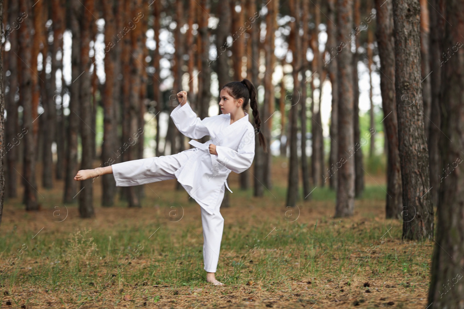 Photo of Cute little girl in kimono practicing karate in forest