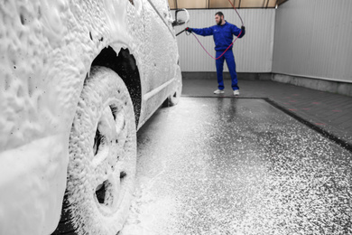 Photo of Worker covering automobile with foam at car wash, focus on wheel