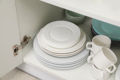 Photo of Clean plates and cups on shelf in cabinet indoors