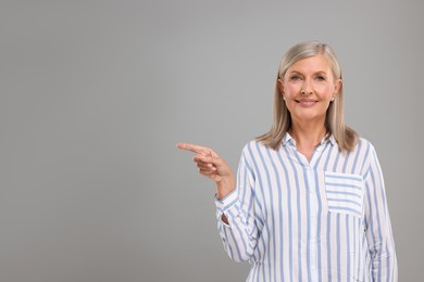 Portrait of beautiful middle aged woman pointing at something on light grey background, space for text