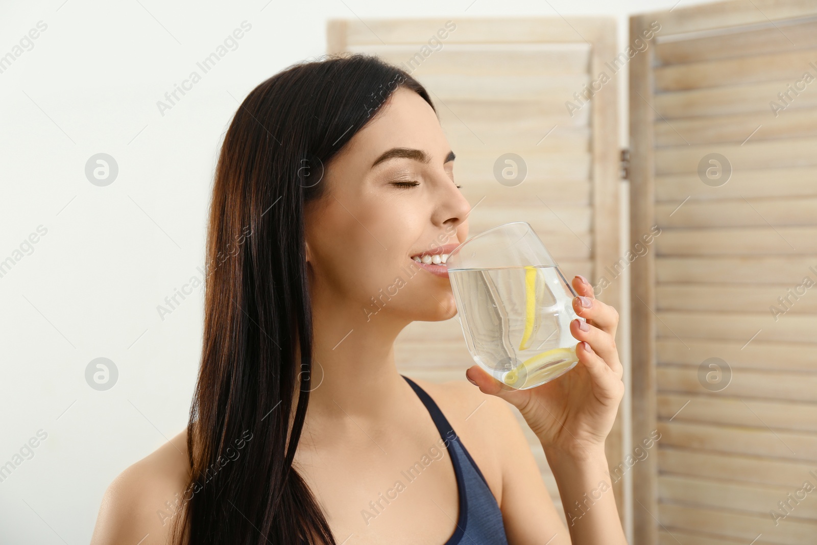 Photo of Beautiful sportive woman drinking fresh lemon water indoors