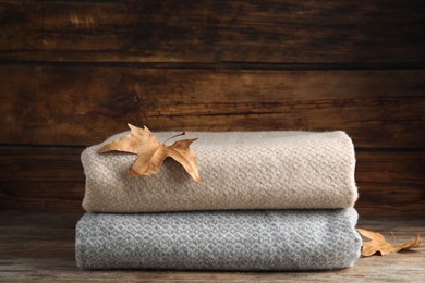 Photo of Grey and beige plaids with dry leaves on wooden table, closeup